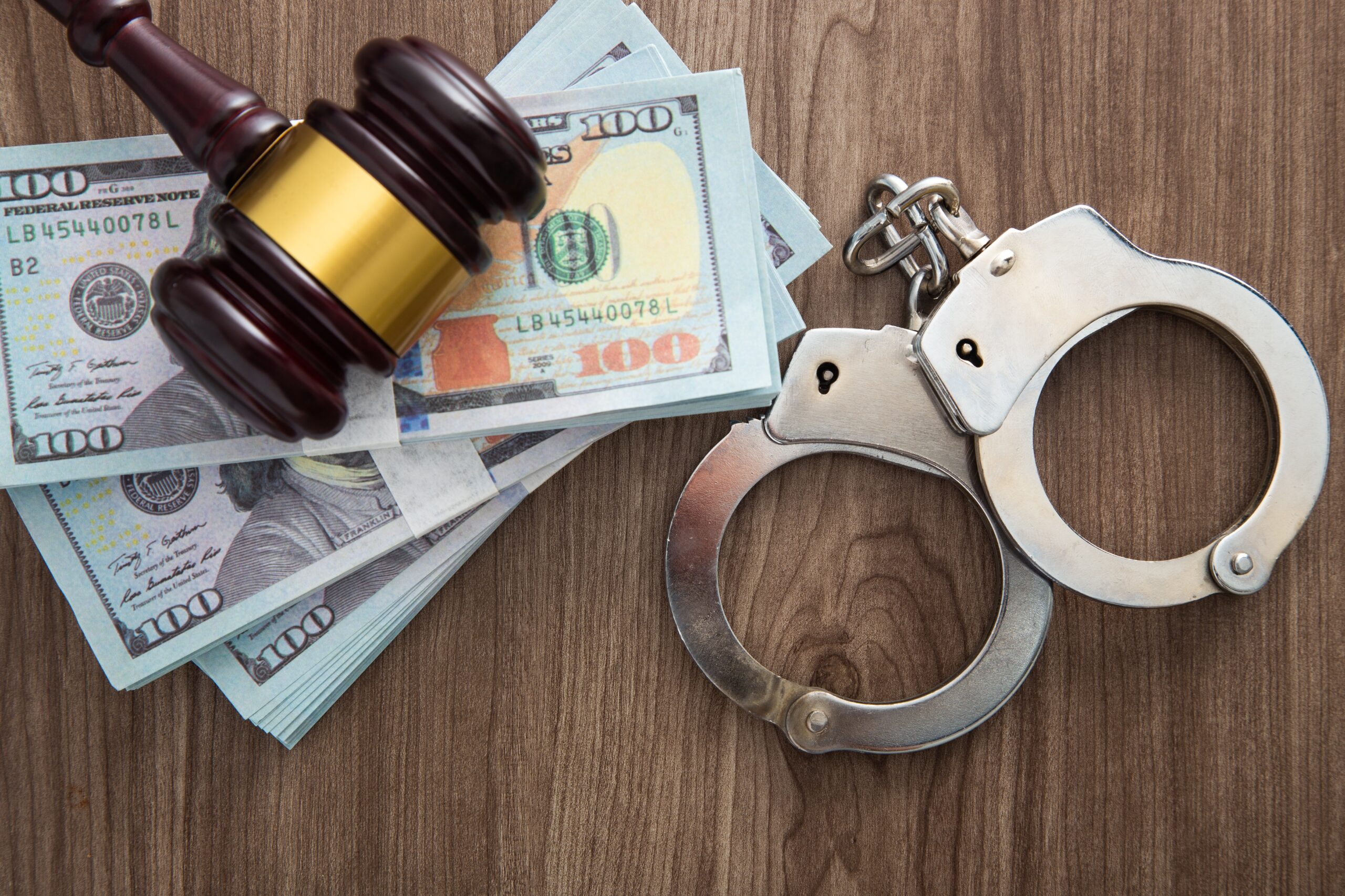 A judge’s gavel, handcuffs, and stacks of U.S. dollars symbolizing the link between money and incarceration.